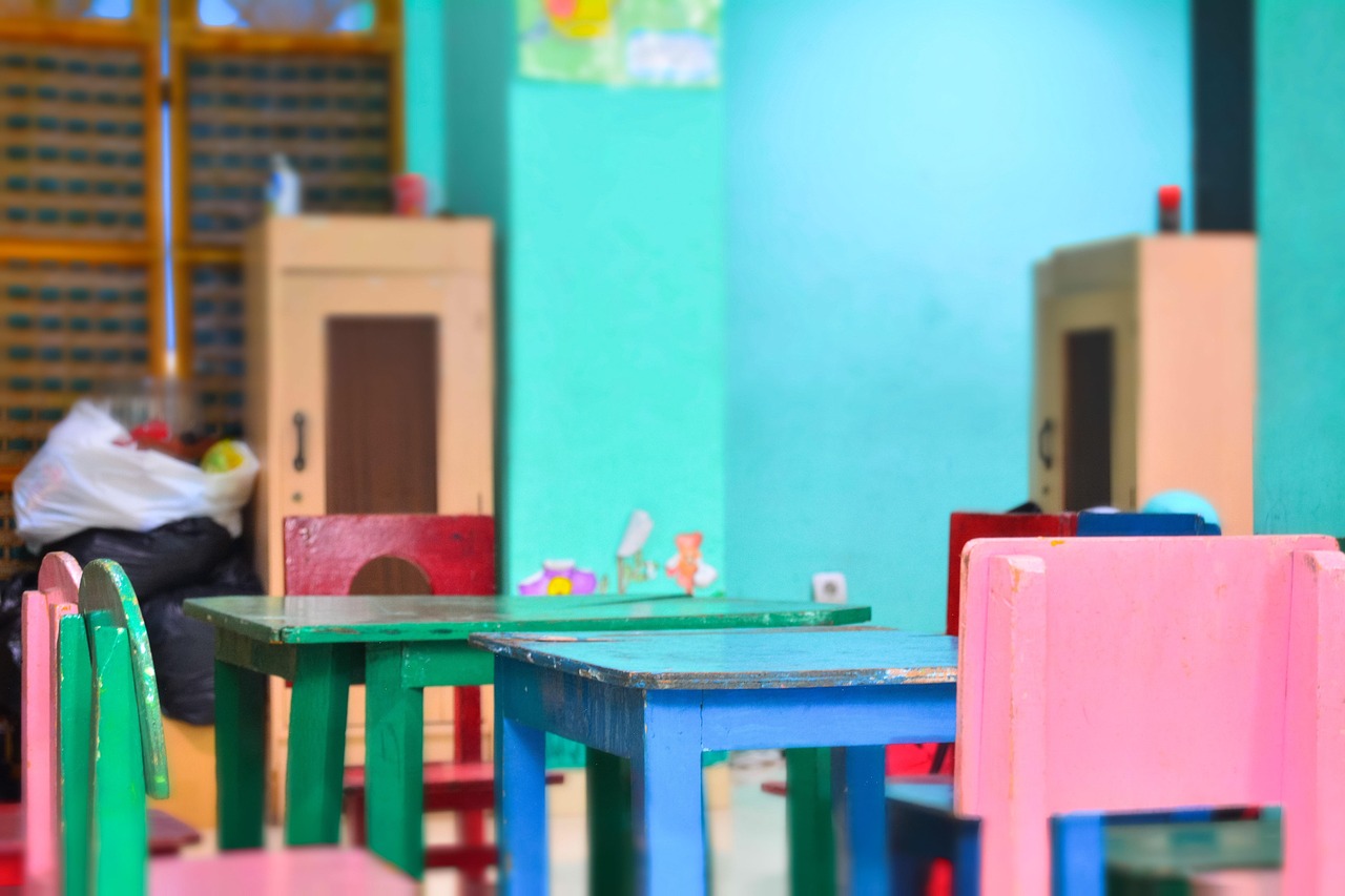 A colorful, empty classroom with small tables and chairs for young children.