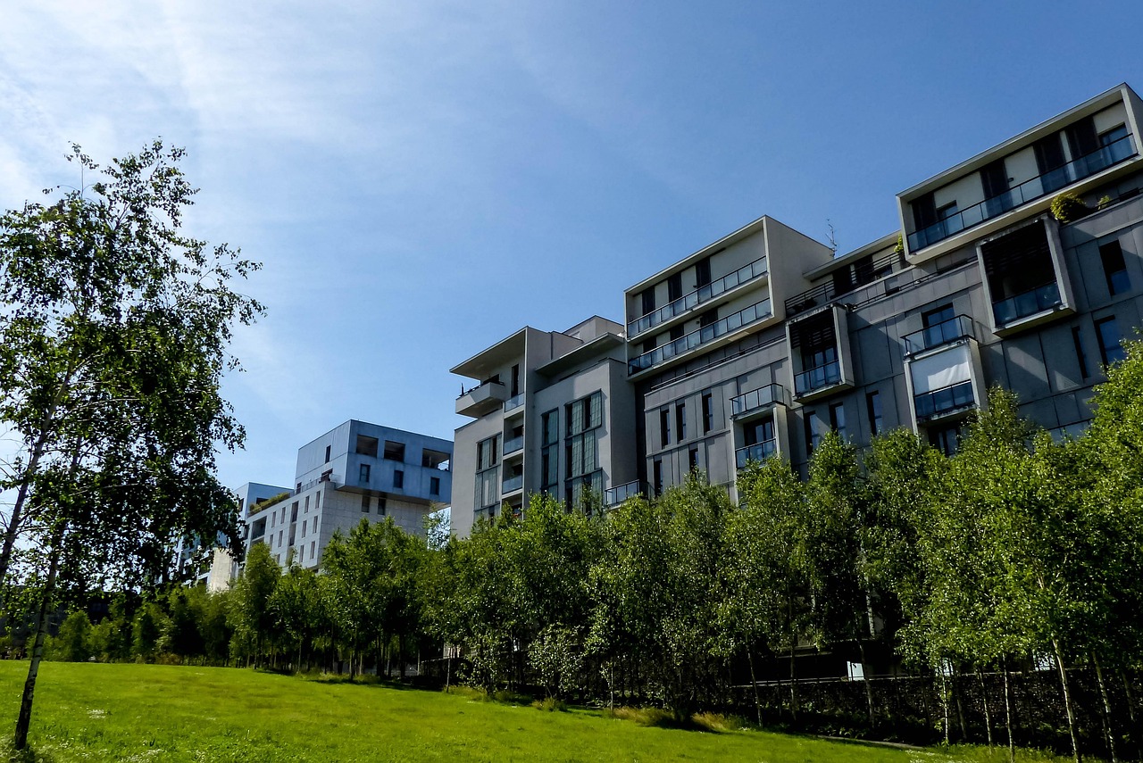 A modern residential apartment building with balconies, surrounded by trees and a green lawn.