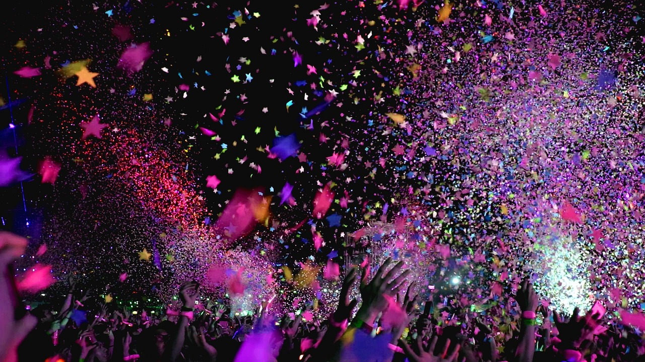 A crowd at a concert with colorful star-shaped confetti falling in the air.