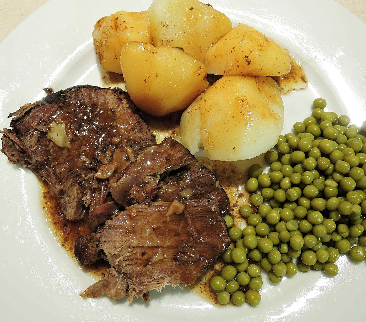 A plate of pot roast with potatoes and peas.